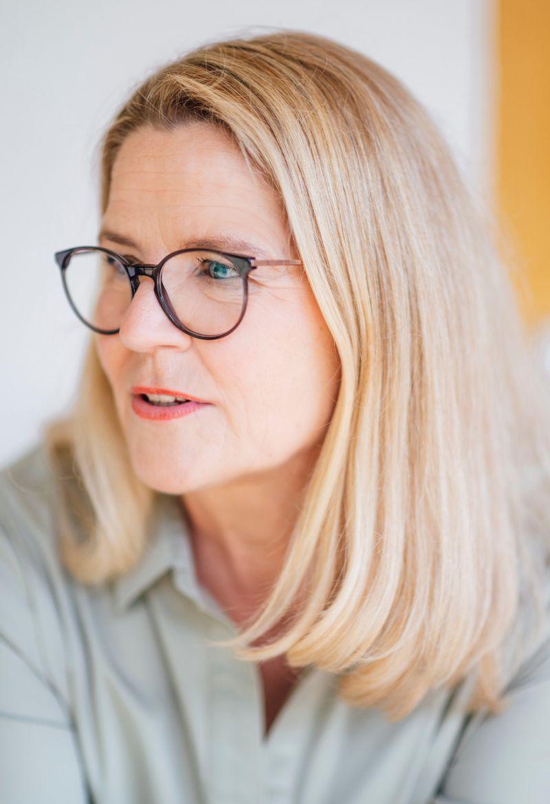 Meike Schüttkus konzentriert im Gespräch, sitzend, leicht nach vorne gebeugt.